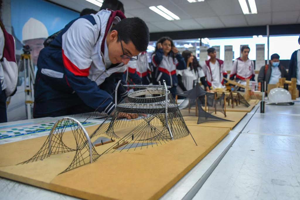 Estudiantes miran las maquetas de diferentes edificaciones mientras les explican qué es el programa de Arquitectura